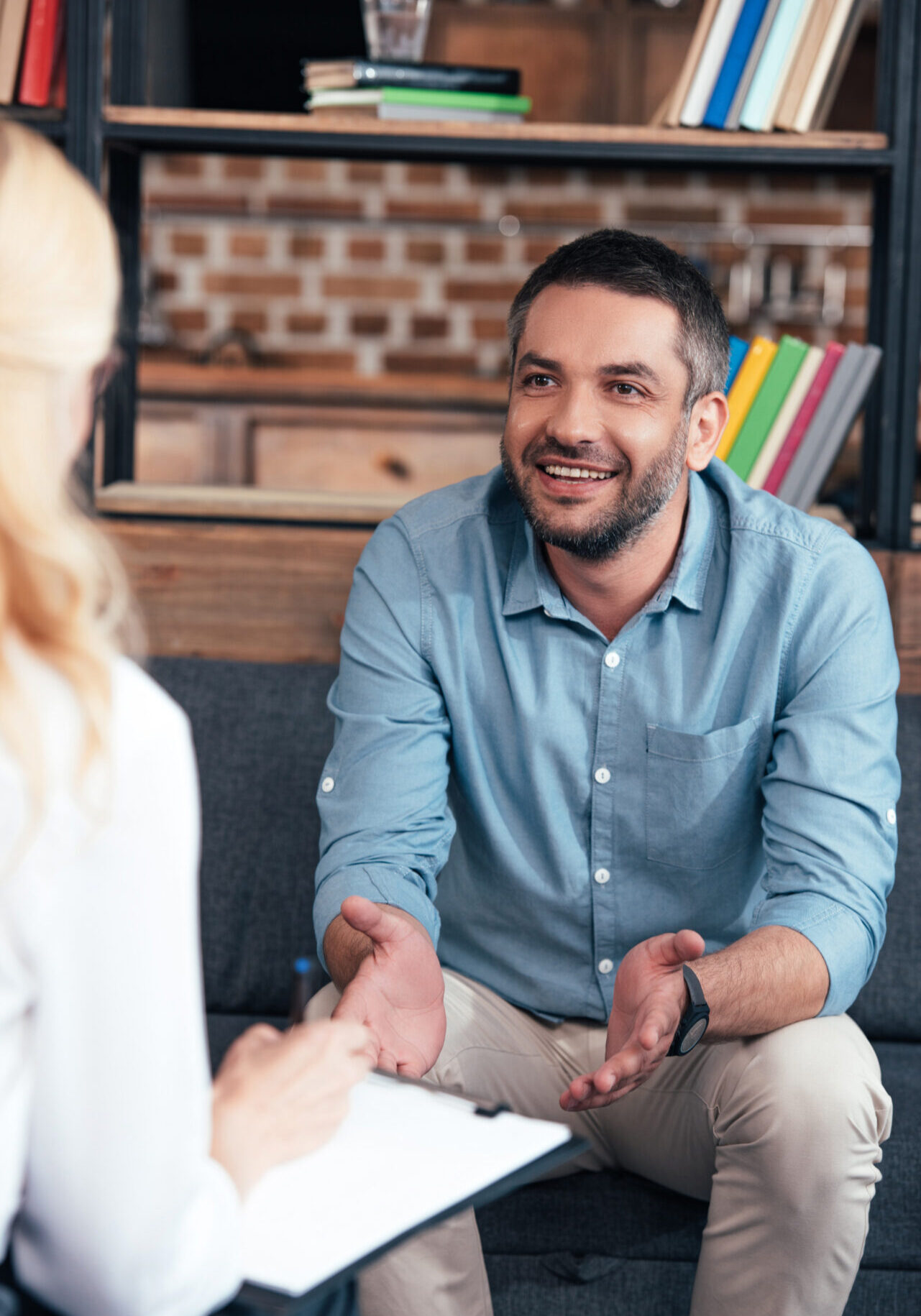 cropped image of female psychiatrist writing in clipboard and talking to smiling man gesturing by hands in office